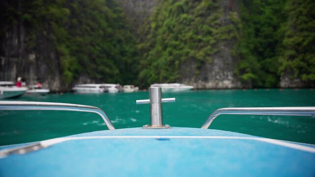 Blue speedboat bow with metal cleat and chrome railings floating in turquoise waters at Ao Pi Le near Loh Samah Bay and Maya Bay in Phi Phi Thailand with limestone cliffs.