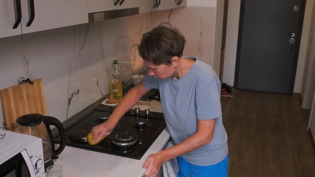 Woman cleaning metal gas stove with cloth, removing grease, stains and dirt from burners and surface, maintaining hygiene and cleanliness in kitchen interior, daily household routine