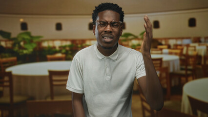 Fototapeta premium African american man wearing white polo shirt raising right hand gesture inside restaurant building; confusion.