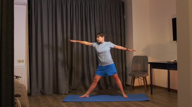 woman entering warrior yoga pose side view, transitioning with light jumps on mat in home interior, practicing balance and flexibility, dynamic fitness routine for strength and body control
