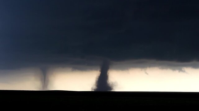 Twin tornadoes under a dark cloud are backlit by the sun  in this time lapse video.