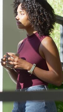 Vertical video: Holding mug by window woman in maroon top feeling sun adjusting grip closing eyes