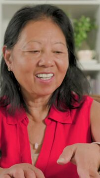 Vertical video: Smiling senior woman in red top tapping phone after message at table sipping water