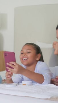 Vertical video: Guiding mother, aunt leaning on bed, helping girl with brush and pink phone smiling