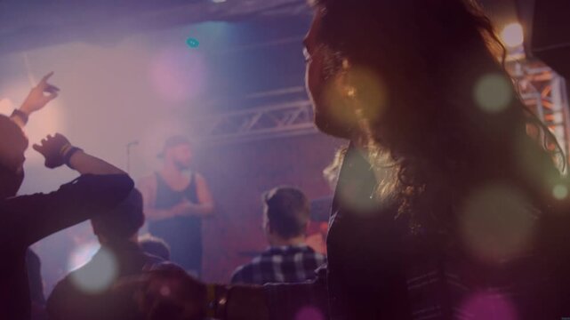 Back crowd reacting to performer pointing in music venue, lights animating lensflare bathing crowd