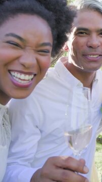 Vertical video: Leaning woman laughing, couple wearing white toasting flutes in park showing ring