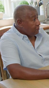 Vertical video: Responding to off-frame cue, man in blue shirt gesturing at kitchen table with mug
