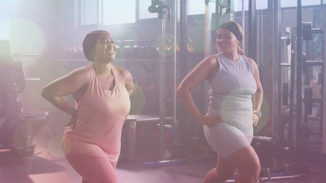 Two women performing lunges in fitness studio with lens flare, starting lunge and finishing set