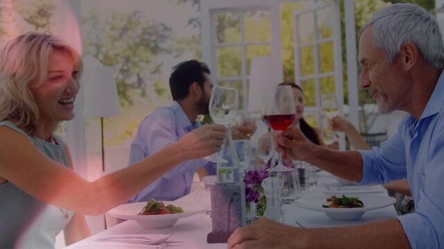 Lead couple making eye contact and clinking wine glasses in dining sunroom, starting group toast
