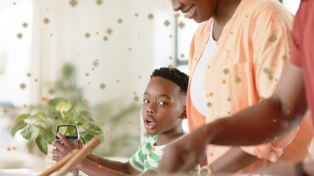 Boy holding peeler at counter, parents chopping vegetables for meal, sparkles floating across scene