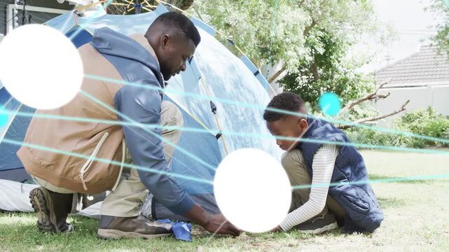 Father and son placing stake, securing blue tent for camping, teal overlays sweeping hands