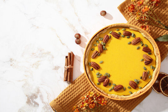 Homemade pumpkin pie on marble with pecans and spices