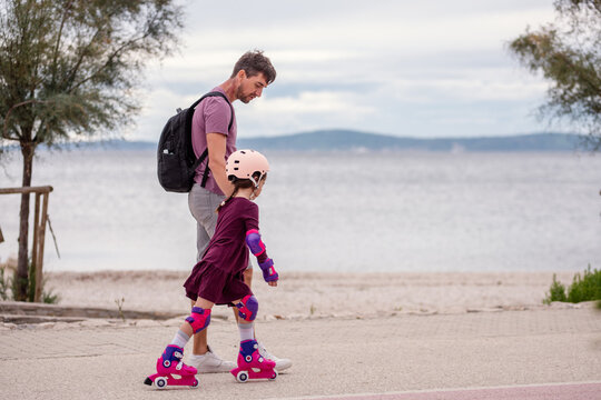 Father teaching daughter roller skating by seaside