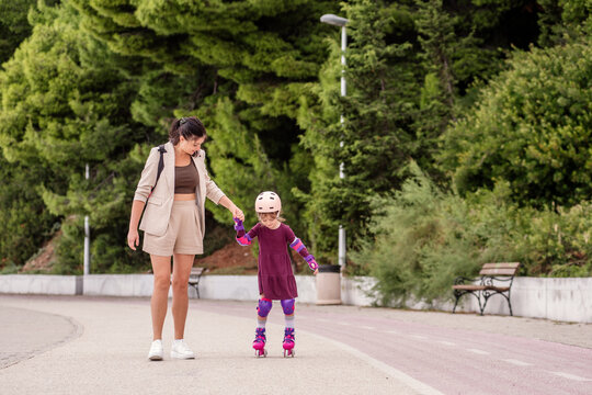Mother teaching daughter to roller skate outdoors