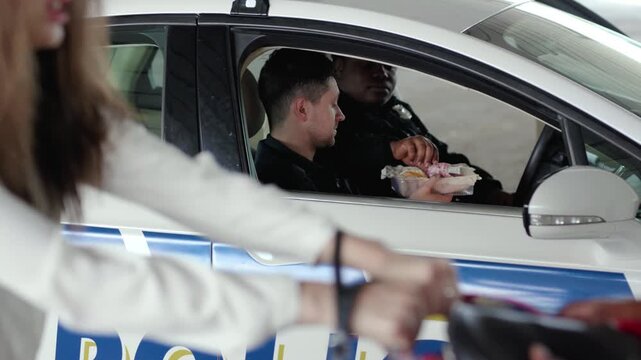 Young two policemen eating donut smile talk see how a man steals a woman's bag near patrol car help happy african american break rest gangster uniform funny teamwork portrait slow motion