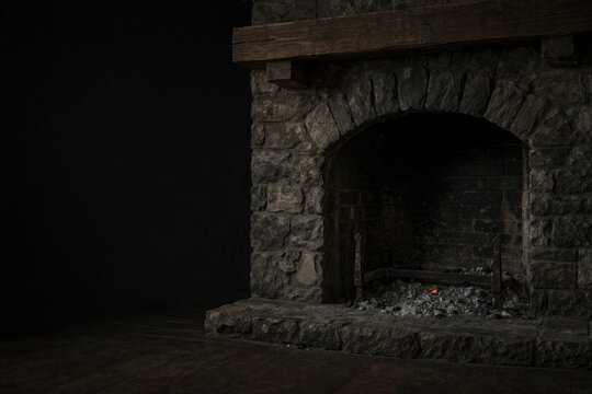 A stone fireplace with glowing embers in a dark room. Space for text.