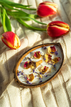 Spa coconut candle with dried petals on cozy blanket