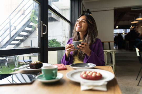 Happy woman enjoying coffee time in modern cafe by window