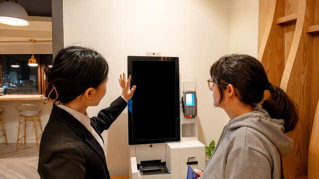 Taiwanese hotel receptionist assisting guest at check-in kiosk