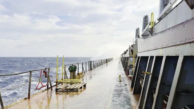 bulk carrier vessel proceeding in a stormy weather. waves get on to the deck and awash cargo hatch coamings. spray, drops, foam, wind. ship construction