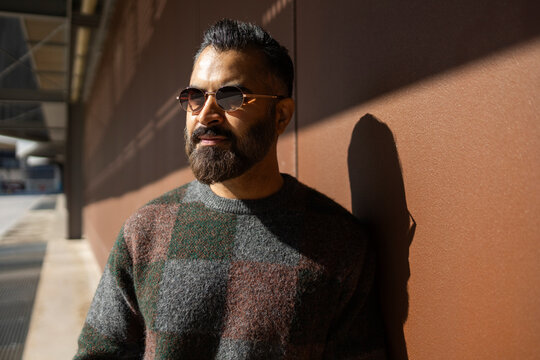 Arab man in sunglasses leaning on wall in sunlight