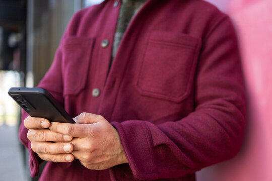 Man using smartphone while leaning on a pink wall outside