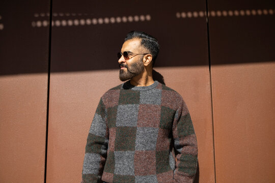 Stylish Arab man in sunglasses by modern wall in sunlight