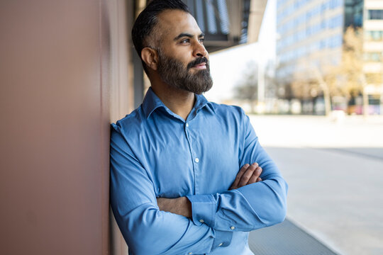 Confident Arab businessman leaning on wall in city office