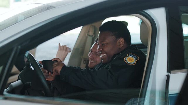 Funny time two policemen eating donut use phone smile talk sitting in patrol car help happy african american break rest gangster uniform funny teamwork portrait slow motion