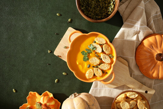 Pumpkin soup with croutons and fresh herbs on green background