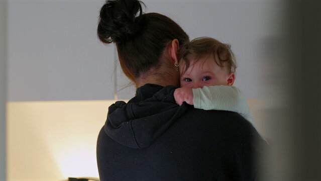 Mother holding baby over shoulder in quiet kitchen, child resting with calm expression, serene domestic moment showing tenderness, safety, and maternal affection