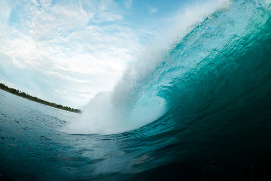 Powerful turquoise ocean wave curling under cloudy sky