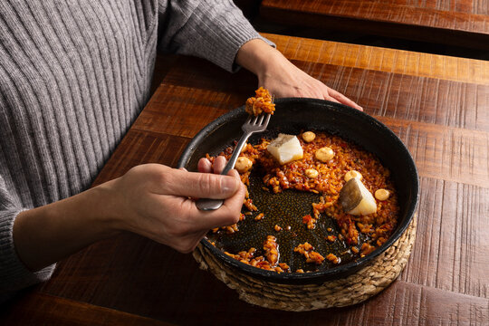 Person eating Spanish rice paella with cod and aioli