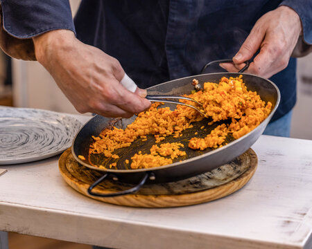 Chef serving Spanish rice from paella pan on table