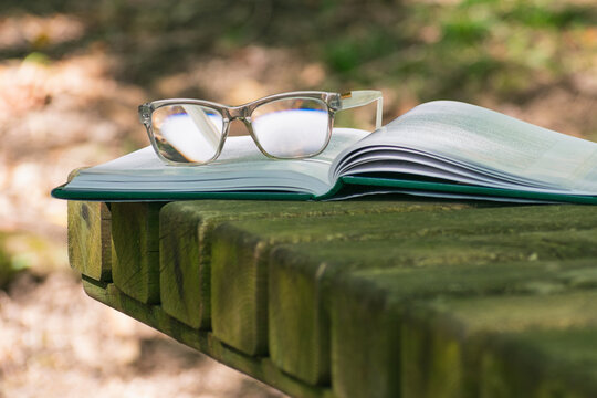 Open book with glasses on wooden table surface