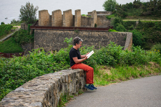 Woman reading by historic stone wall in nature