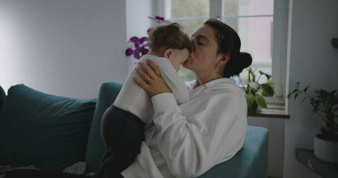 Mother kissing baby affectionately while holding him close in cozy home setting, showing tenderness and love