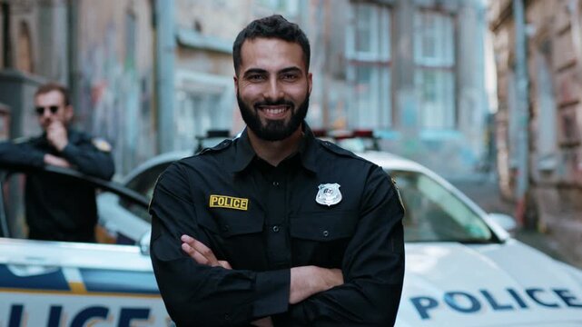 Smiling young man cops stand near patrol car look at camera enforcement happy officer police uniform auto safety security communication control policeman portrait close up slow motion