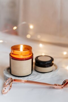 Lit soy candle in amber jar with scissors and bokeh