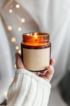 Woman's hand holding lit soy candle in brown glass jar