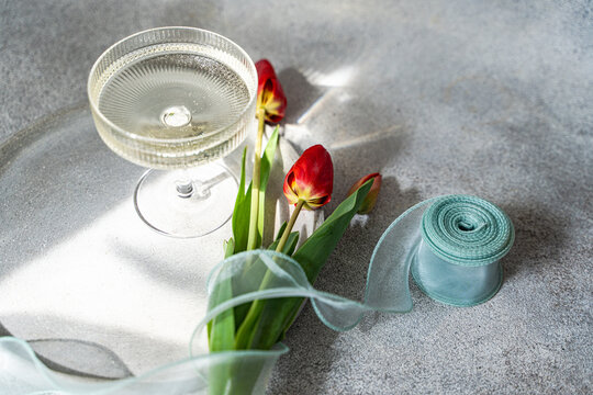 Red tulips on table with glassware and ribbon in light