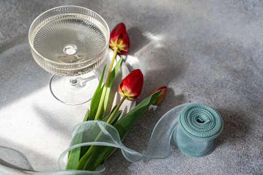 Red tulips on table with glass and ribbon in soft light