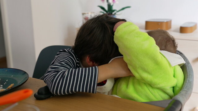 Older brother interacting with baby sibling during lunch time at home, showing gentle affection, playful connection, and tender family bonding between children