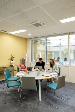 Coworking team working on laptop around table in office