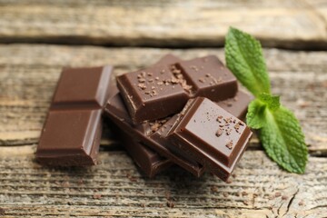 Pieces of yummy chocolate and mint leaves on wooden table, closeup © New Africa