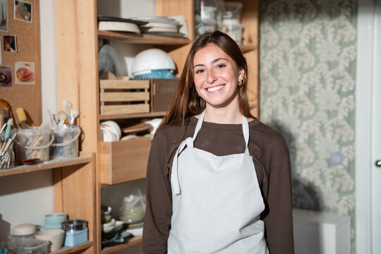 Smiling potter in apron standing in pottery studio
