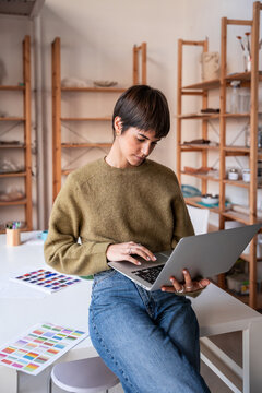 Ceramic artist using laptop in pottery workshop studio space