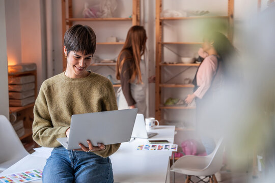 Young artisan manager using laptop in pottery workshop studio space