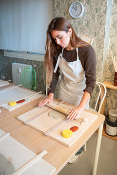 Young woman shaping clay with rolling pin in pottery studio