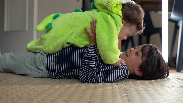 Older brother lying on floor lifting baby in green outfit, joyful sibling play showing laughter, affection, and family bonding